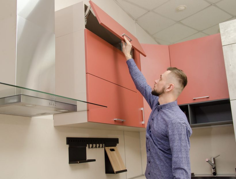 Attractive bearded man closes the top cabinet drawer in a modern kitchen.