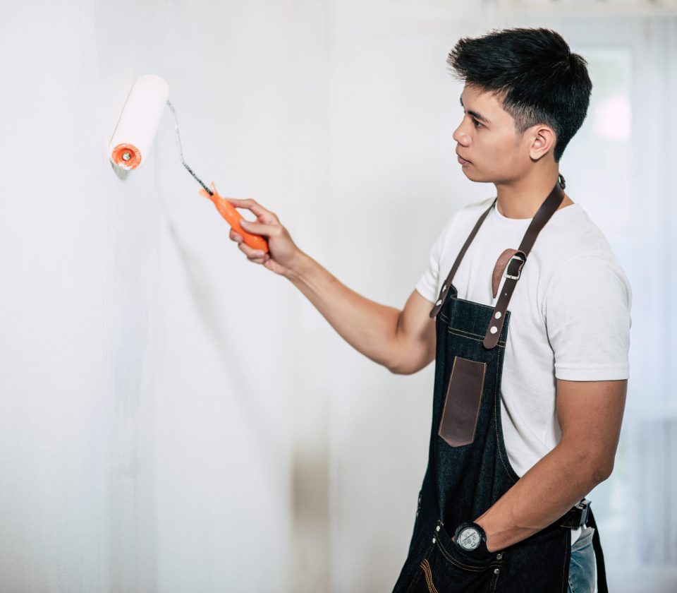 A carpenter holds a paintbrush and paints wood. Selective focus.