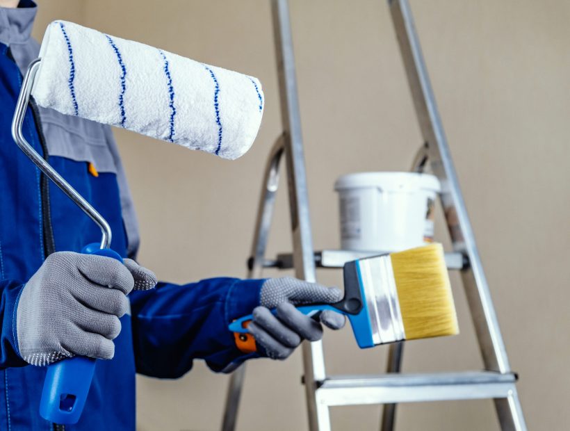 The plaster painter is ready to paint the wall. In the hands of a roller and brush. A stepladder and a bucket of paint in the background